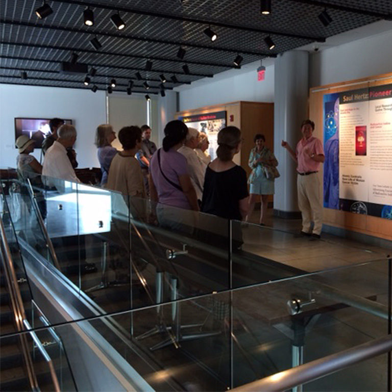 man in pink sur speaking to group of people leaning against a glass staircase wall