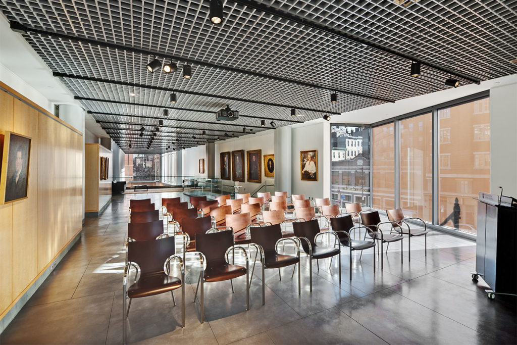 Five rows of wooden chairs facing podium with large portraits of white men in background