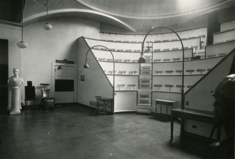 B&W photo of interior of amphitheater with view of steps; old OR chairs and stone bust in background