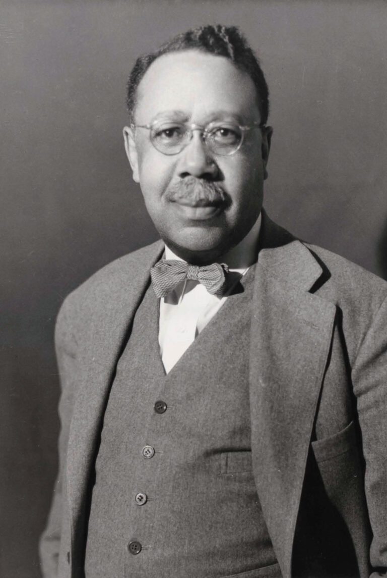 black & white photo of man wearing grey suit, a bow tie, and glasses