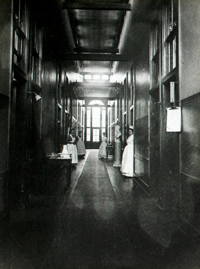 black & white photo hallway with two nurses standing at doorways on each side