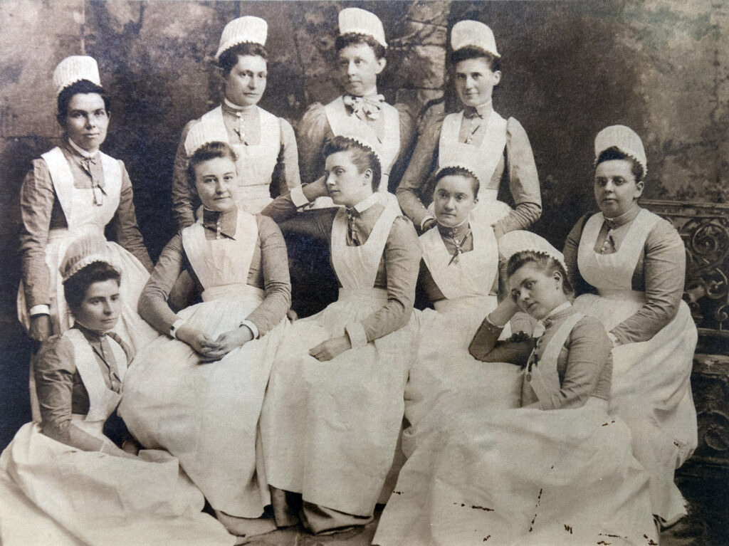 Sepia-toned group portrait of ten seated women wearing identical nurse uniforms