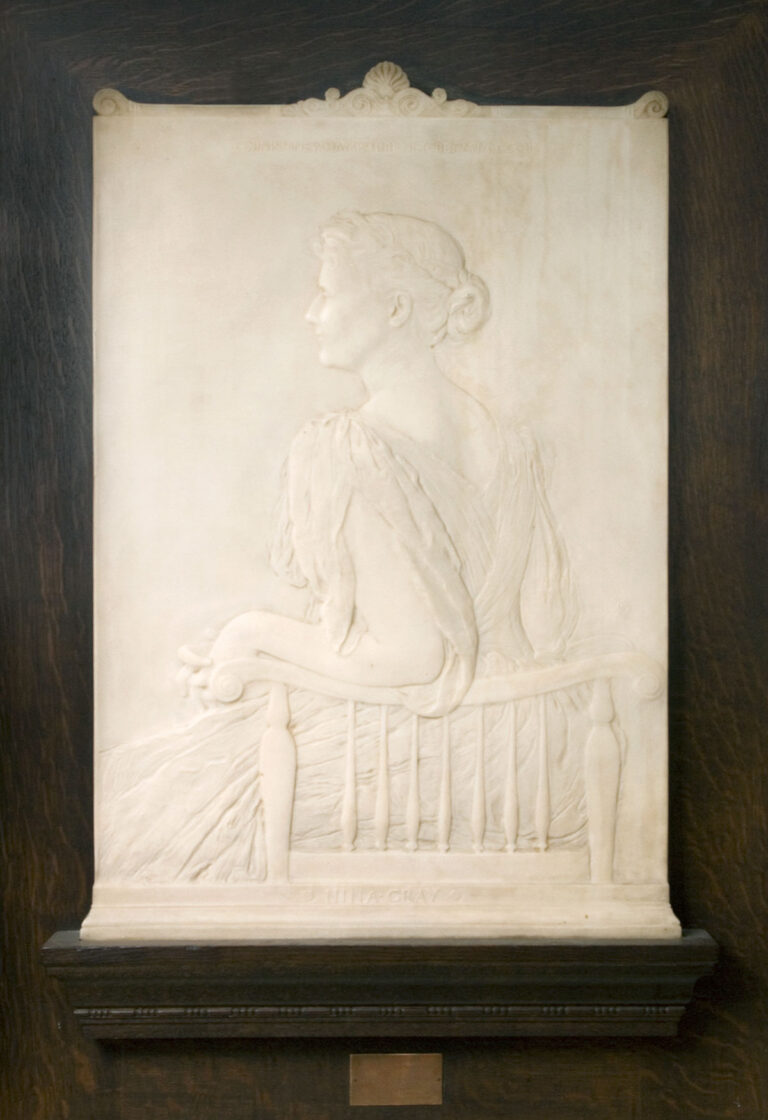 White marble bas-relief portrait of a woman in profile with her arm resting on a backrest of a chair