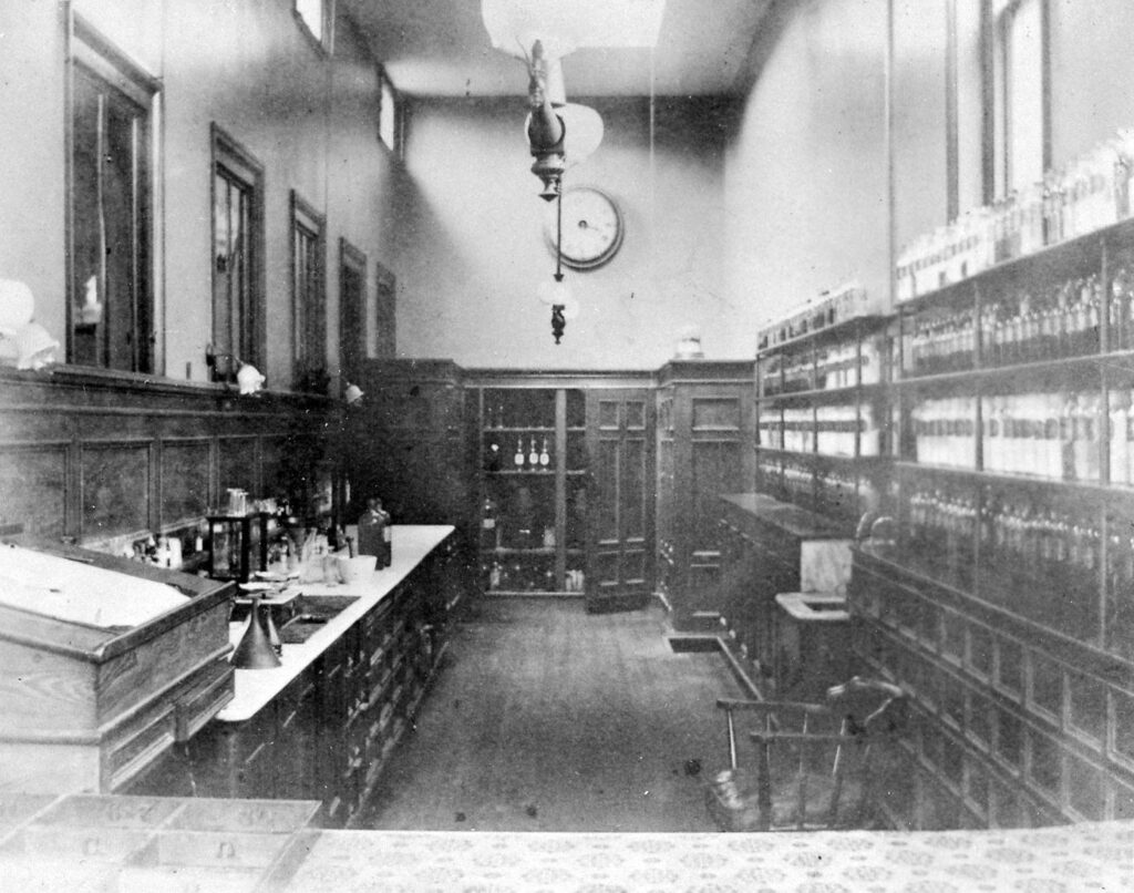 black & white photo of apothecary room with several jars lining the wall on the right