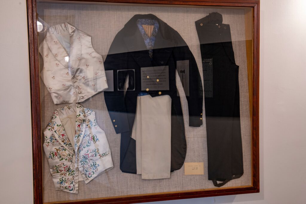 vests, a coat, and two pairs of pants in a flat, wall-mounted glass case