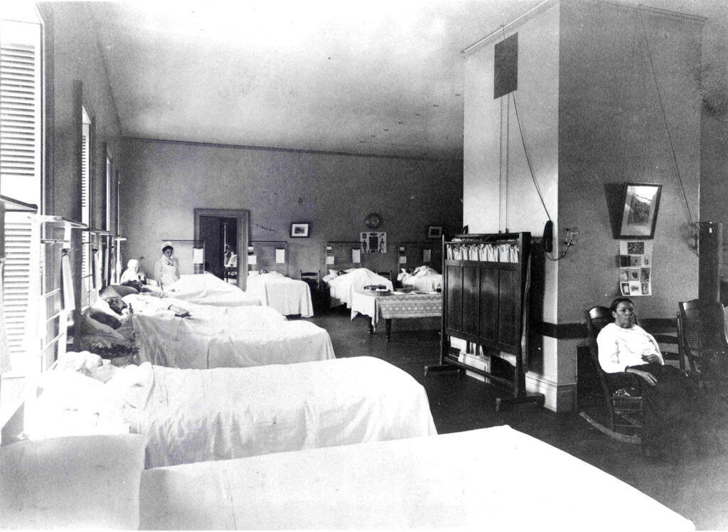 Women lying in beds. One woman on the right is sitting in a rocking chair.