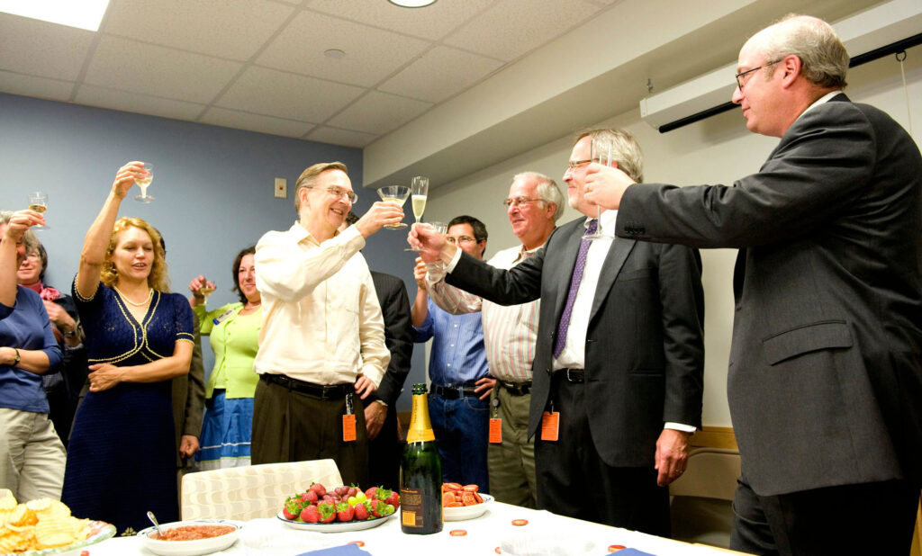 color photo of several people around a conference room table, raising glasses of champagne