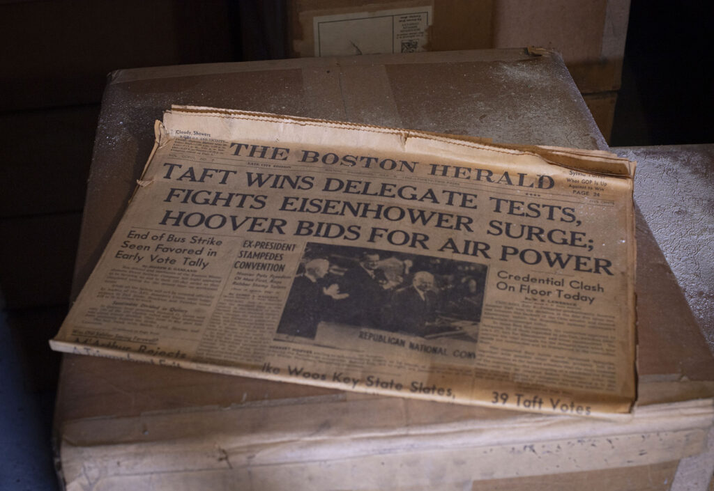 An old copy of the Boston Herald lies on top of box, surrounded by other cardboard boxes with plaster dust. Headline reads: TAFT WINS DELEGATE TESTS, FIGHTS EISENHOWER SURGE; HOOVER BIDS FOR AIRPOWER"